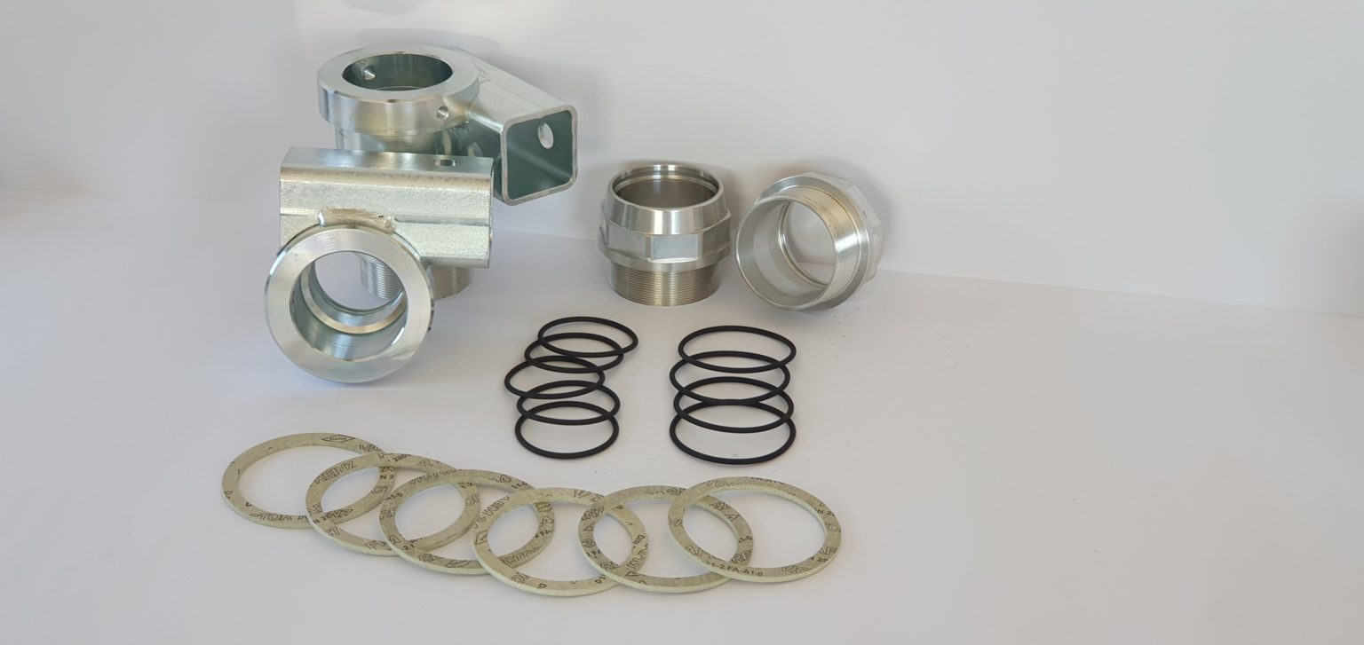 Metallverschraubungen, Ersatzteile, O-Ringe und Dichtungen liegen geordnet auf einer weißen Fläche vor neutralem Hintergrund.