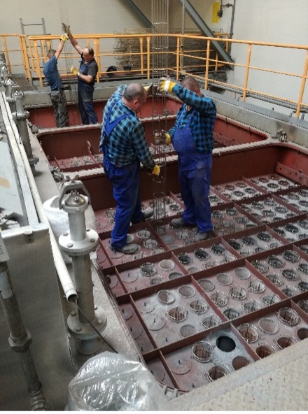 Zwei Arbeiter in blauer Arbeitskleidung montieren Metallstangen in einem Filtertechnik-Tank, zwei weitere arbeiten im Hintergrund.